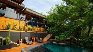 A modern house with a pool, wooden deck, and lush greenery.