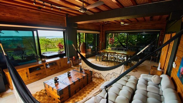 A spacious living area with a hammock, a large sofa, a wooden coffee table, and a dining table.