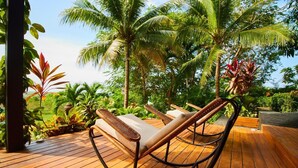 A wooden deck with a rocking chair and lush tropical plants.