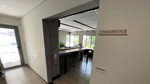 A modern coworking space with a clean, minimalist design, featuring a kitchen area, bar stools, and a sign indicating the coworking area. - Brooklin subway - US Consulate - Vibra São Paulo (Jardim das Acacias São Paulo)
