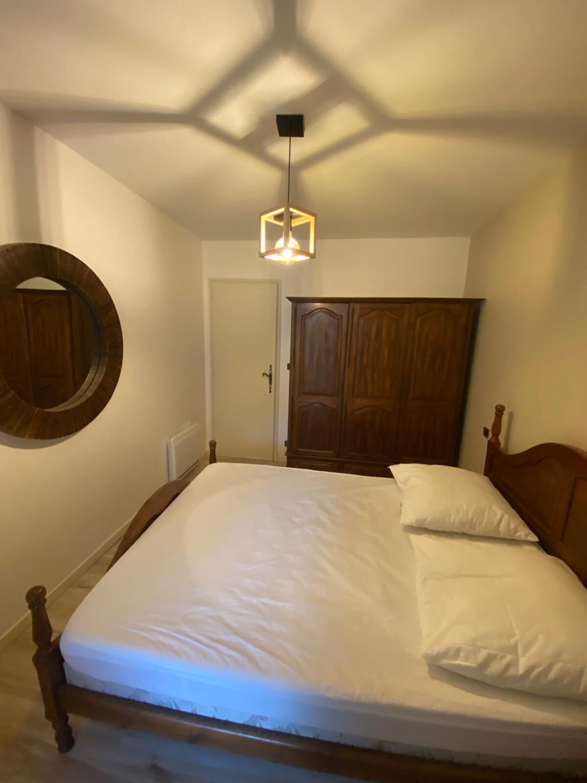 Une chambre à coucher avec un lit en bois, un miroir rond, une armoire et un luminaire suspendu.