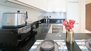 Una cucina moderna con un piano di lavoro nero, un bollitore, un forno a microonde e un vaso con fiori.