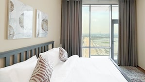 Una camera d'albergo con un letto grande, due opere d'arte a parete, un lampadario moderno e vista sulla città attraverso ampie finestre con tende.