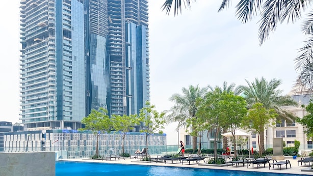 Una piscina con lettini e palme, circondata da edifici alti.