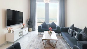Un soggiorno moderno con una TV a schermo piatto, un divano, un tavolino da caffè e un'ampia finestra con vista sulla città.