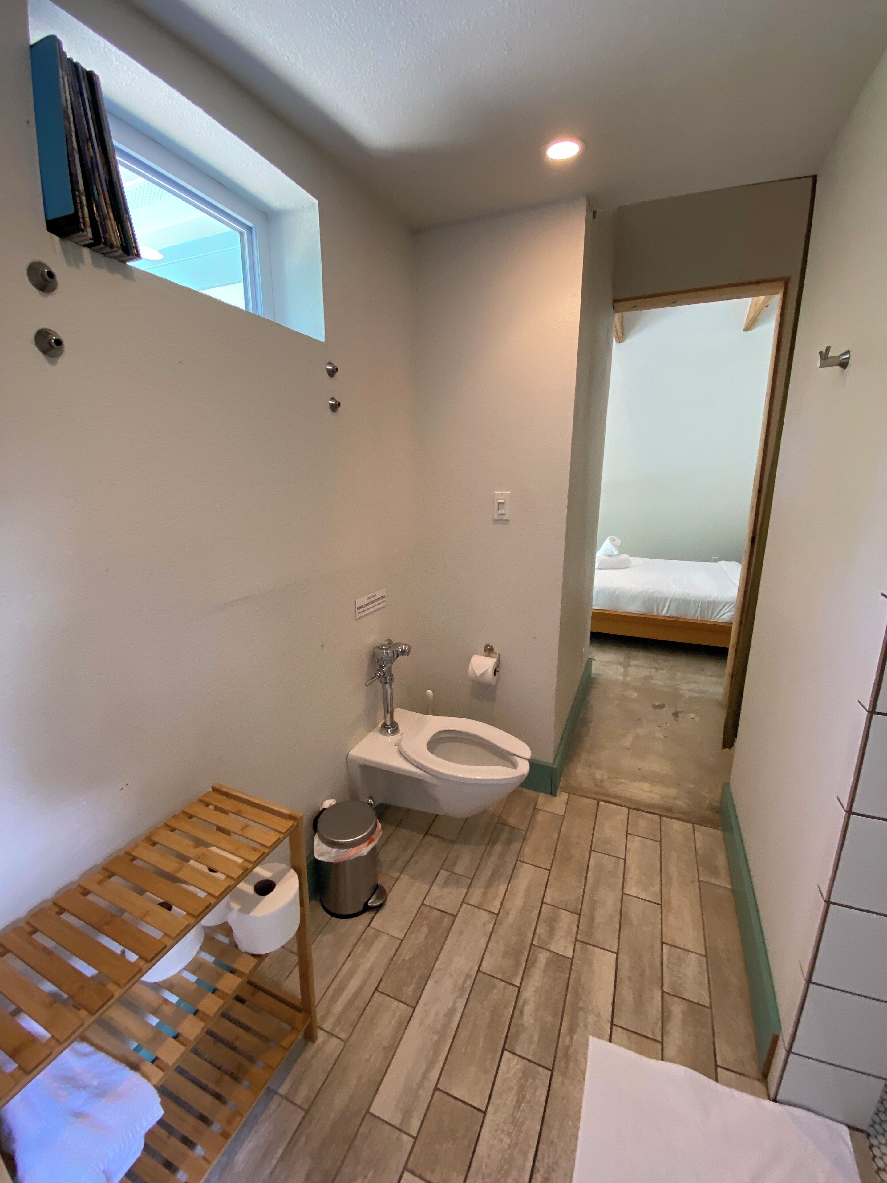 Ein kleines Badezimmer mit Toilette, einem Holzregal und einem kleinen Fenster.