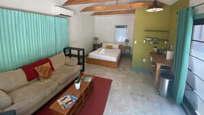 Una sala acogedora con sofá, una mesa de centro con revistas, cama, una mesita de noche con lámpara y una cocina con fregadero y armarios.