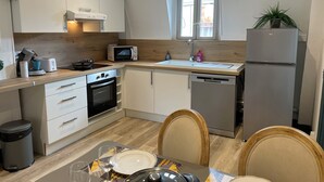 Una cocina moderna con armarios blancos, microondas, fregadero y refrigerador. Hay una mesa de comedor con sillas y una ventana sobre el fregadero.