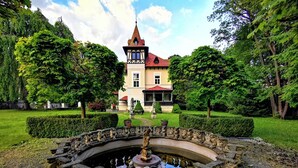 A historic building with a tower, surrounded by a well-maintained garden and a decorative fountain. - Glögglhof (Trofaiach)