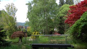 A wooden bridge over a pond, surrounded by lush greenery and trees. - Glögglhof (Trofaiach)