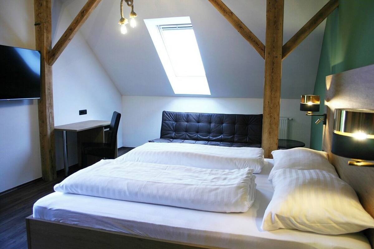 A room with a bed, a desk, and a chair. There is a skylight above the bed.