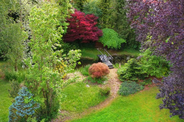 A garden with a pond, various plants, and a wooden bridge.