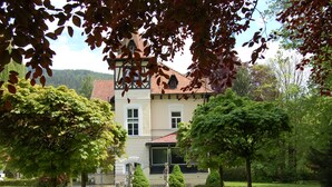A stately building with a symmetrical facade, a central entrance, and a well-maintained garden with hedges and a fountain. - Glögglhof (Trofaiach)