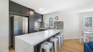 A modern kitchen with a large island, dark cabinets, and a stainless steel refrigerator. - Meridian unit 4 Kings Beach QLD (Kings Beach)