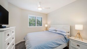 A bedroom with a bed, a TV on a dresser, a ceiling fan, and a window with blinds. - Meridian unit 4 Kings Beach QLD (Kings Beach)