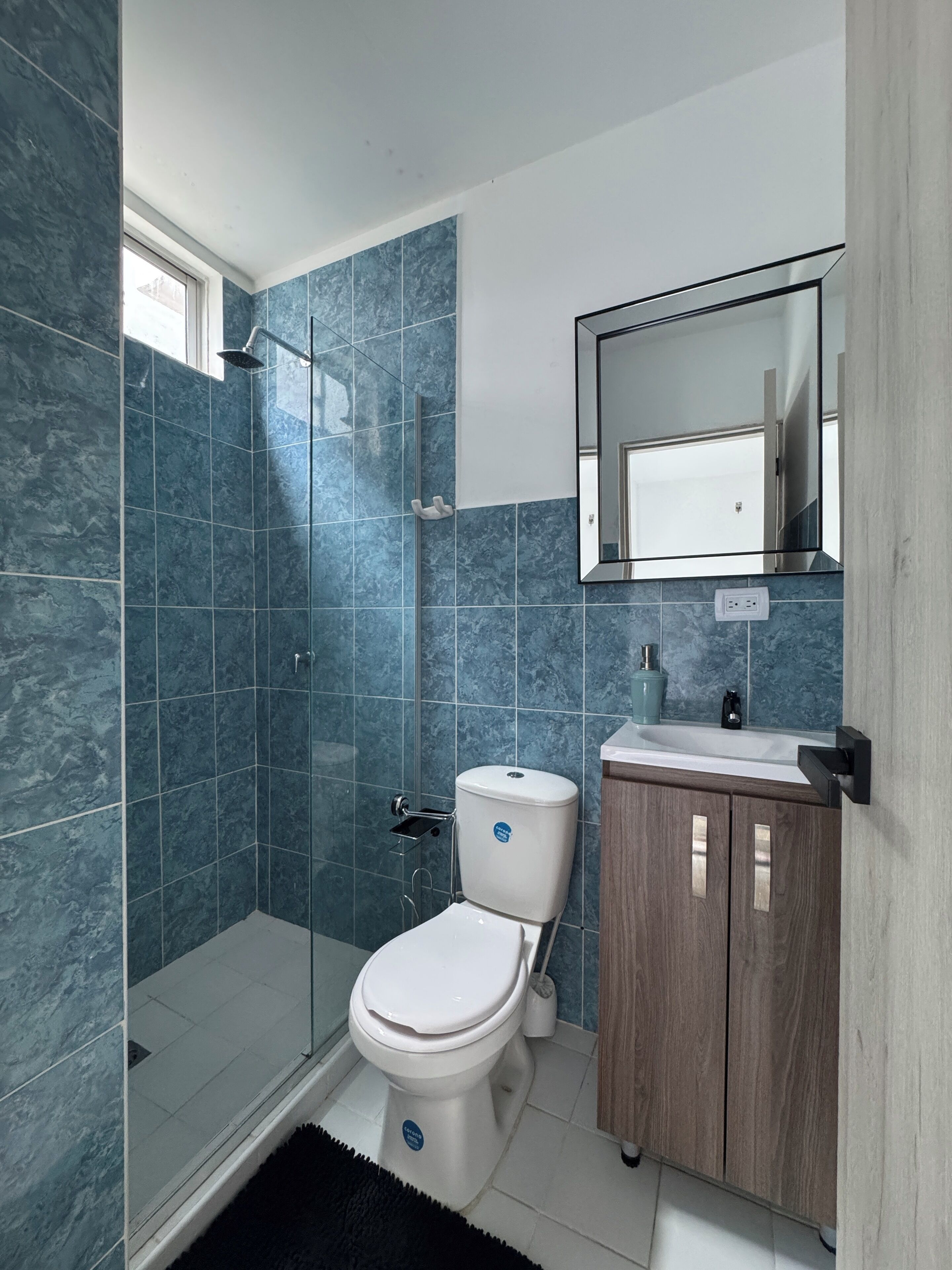 Een moderne badkamer met een douchecabine van glas, een wit toilet en een houten wastafelmeubel met een spiegel erboven.