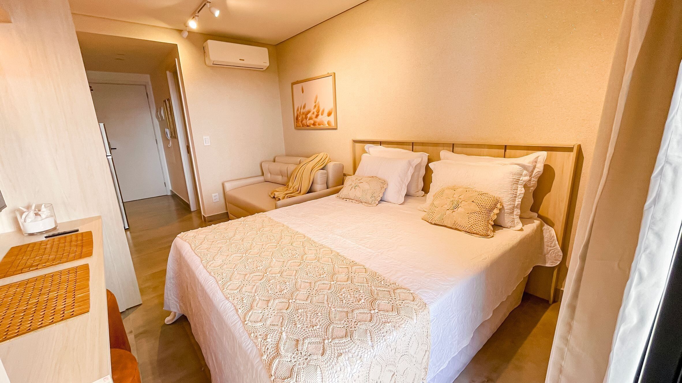 A bedroom with a large bed, a bedside table, a chair, and an air conditioning unit on the wall.