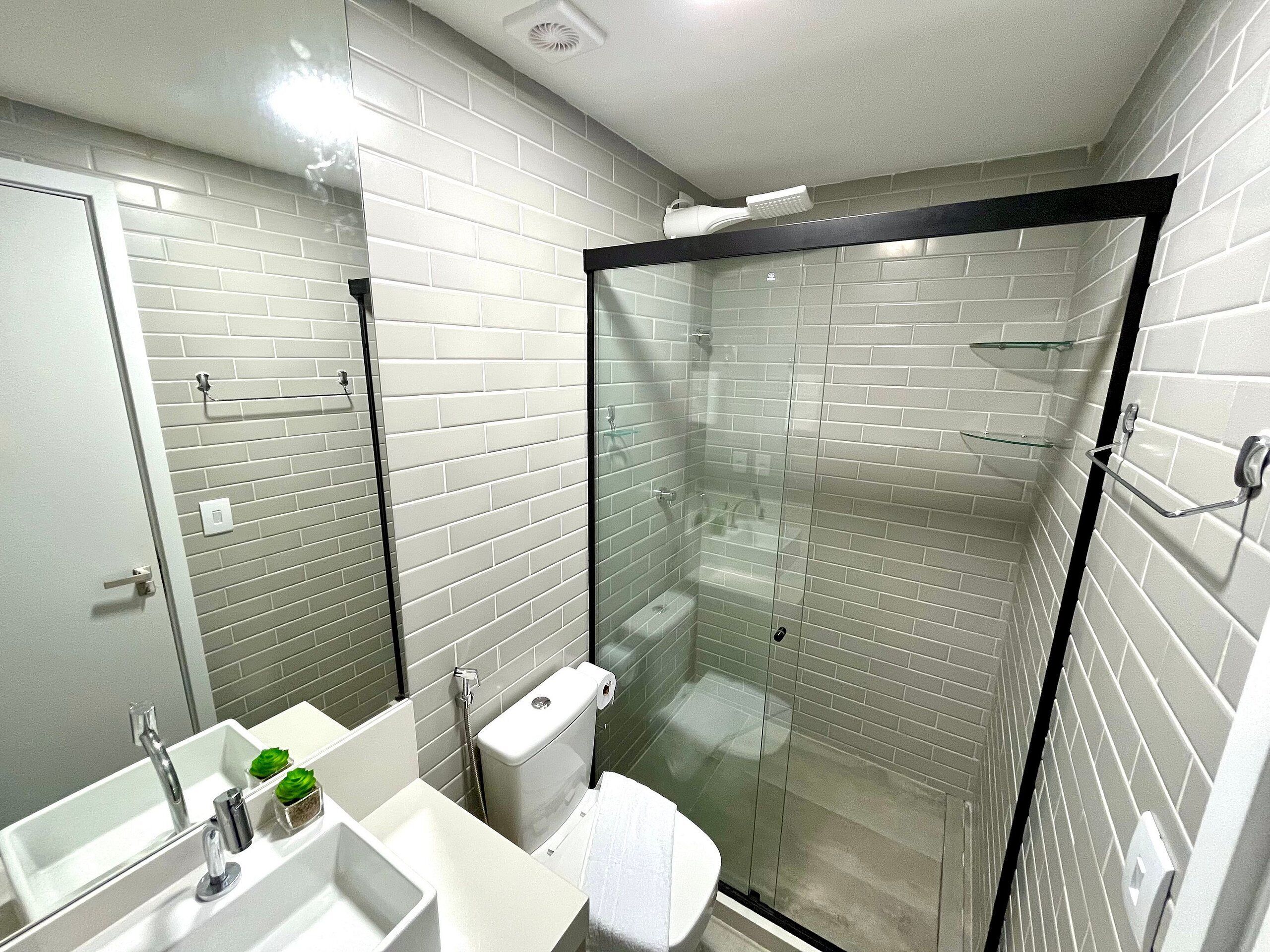 A modern bathroom with a glass-enclosed shower, white subway tiles, and a white sink with a mirror.