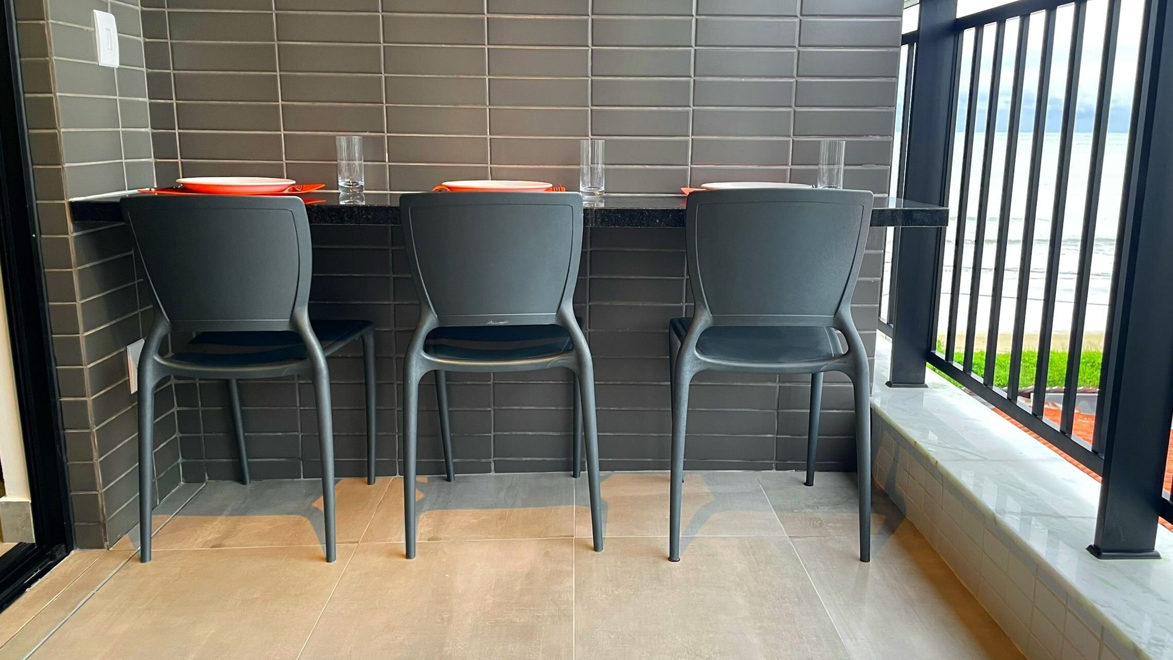 Un coin salon avec trois chaises et une table, un mur recouvert de carreaux et une vue dégagée grâce à une rambarde.