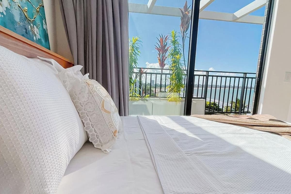 A bedroom with a large bed, a view of the sea, and a balcony with plants.