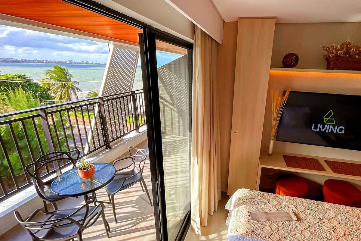 A balcony with a table and chairs, a TV on the wall, and a bed with a patterned bedspread.
