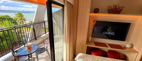 A balcony with a table and chairs, a TV on the wall, and a bed with a patterned bedspread.