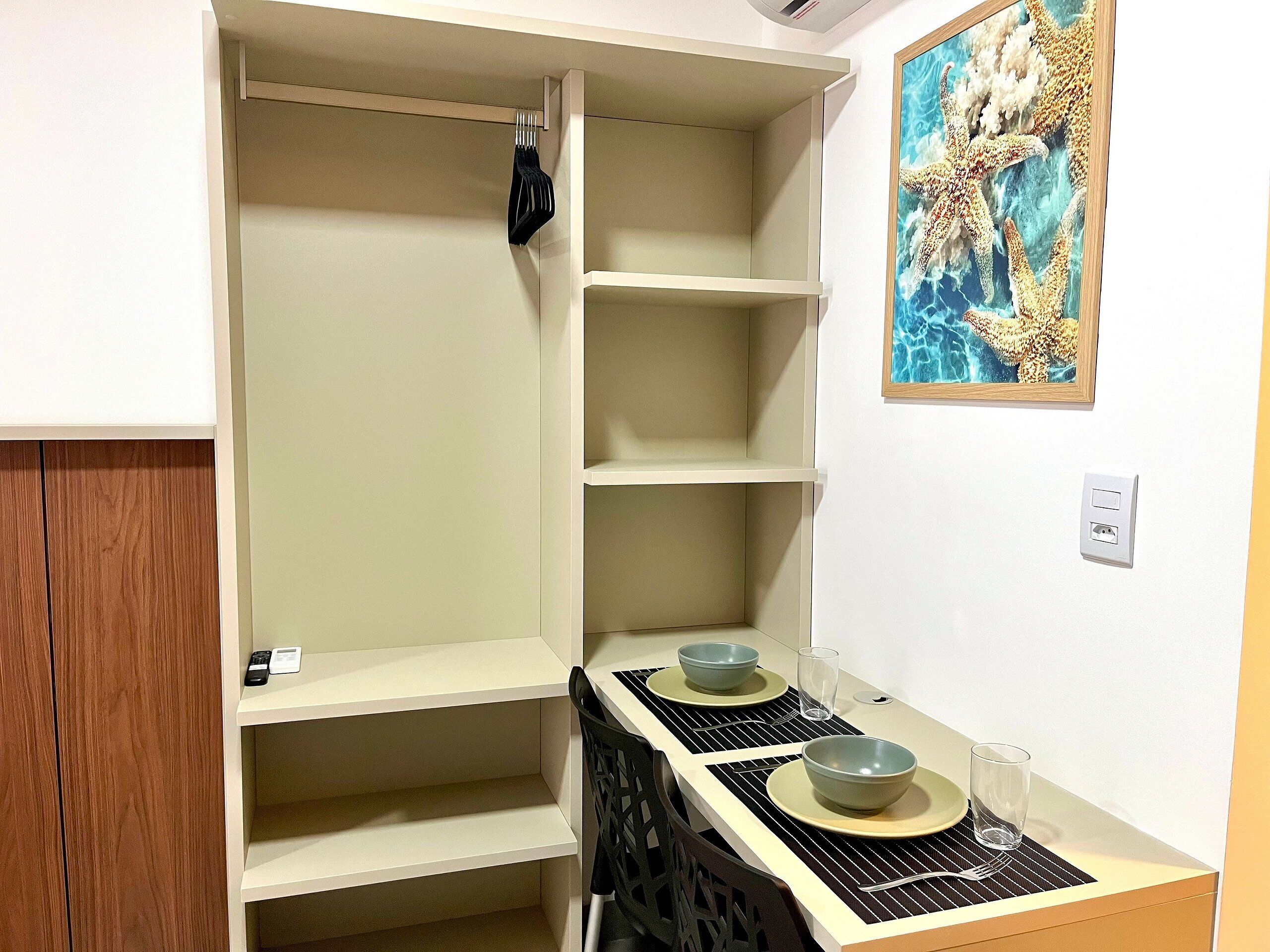 A compact room with a dining table, chairs, a coat rack, and a painting on the wall.