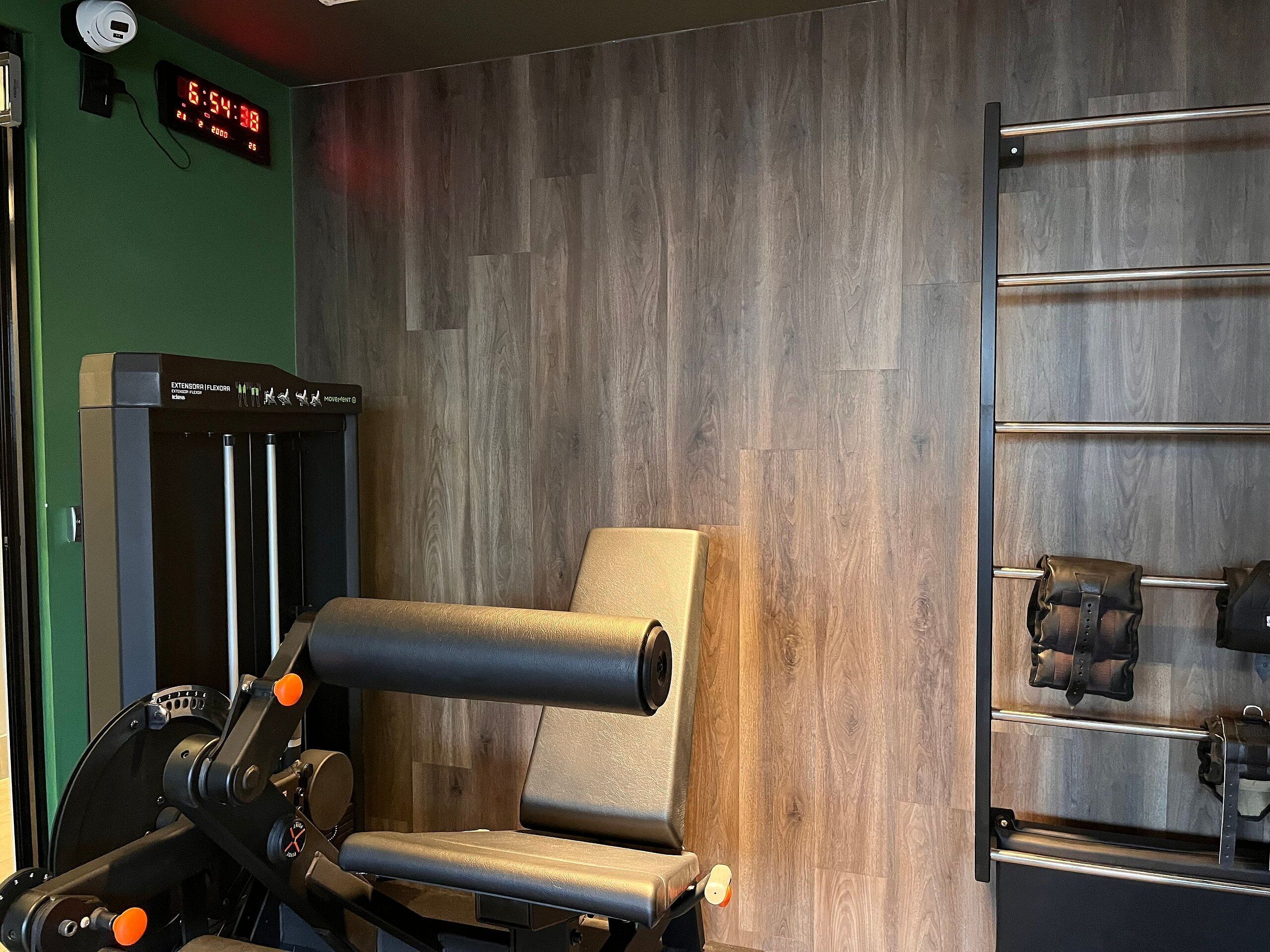A gym with exercise equipment, a digital clock, and a wooden wall.