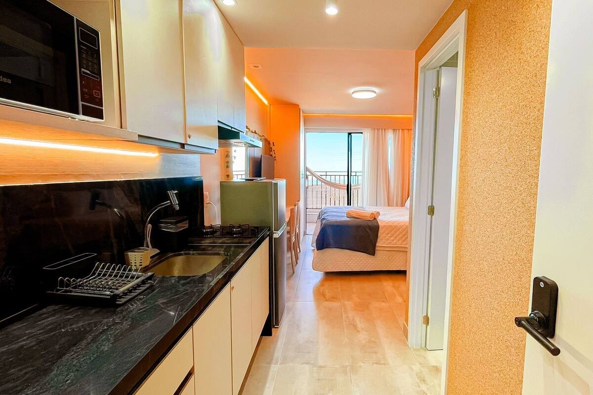 A compact hotel room with a kitchenette, a bed, and a balcony with curtains.
