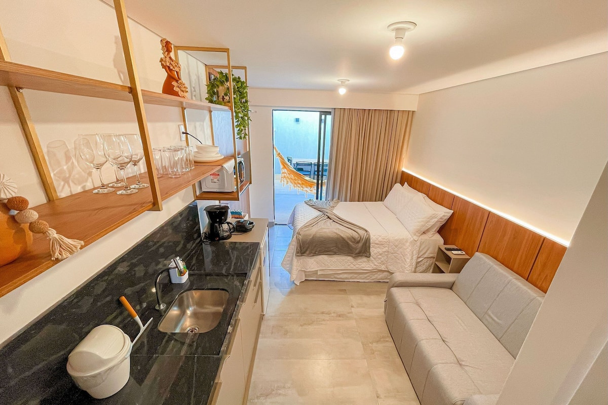 A compact hotel room with a kitchenette, a bed, a sofa, and a view of the outdoors.