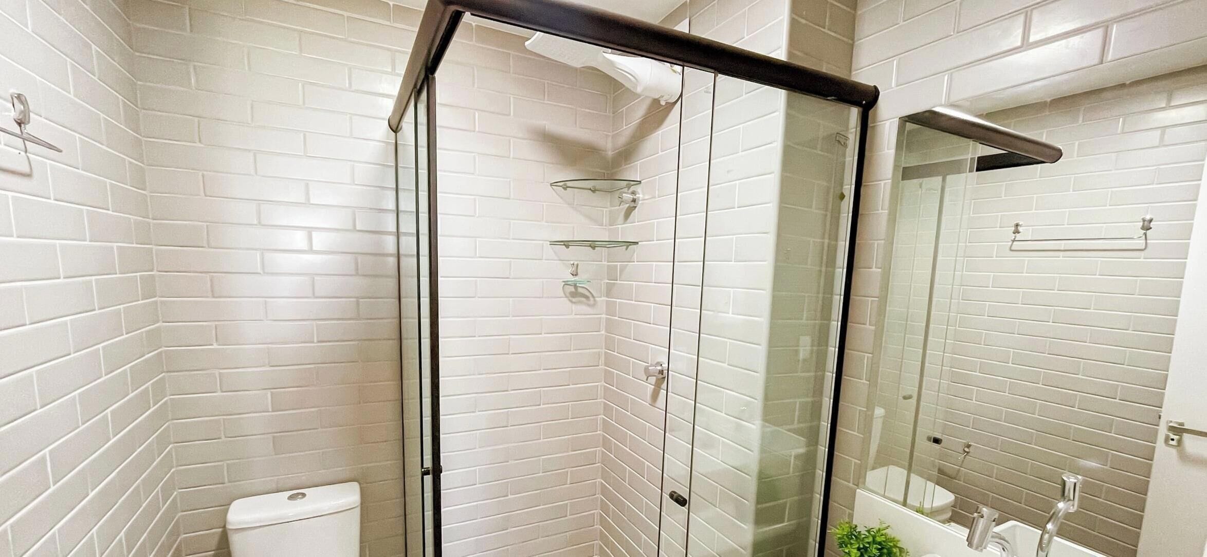 A bathroom with white tiled walls, a glass shower enclosure, and a mirror.