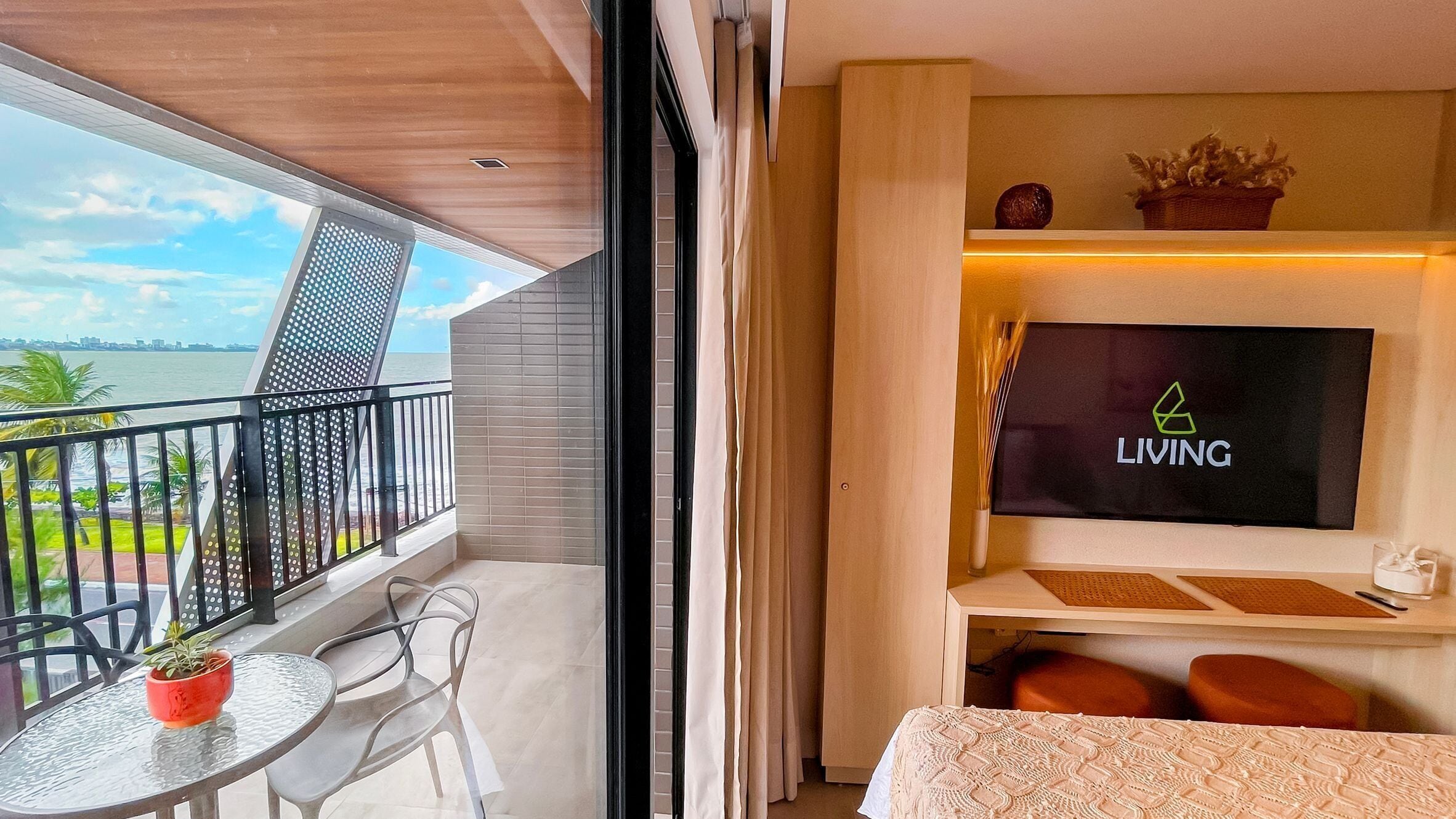 A modern hotel room with a balcony, a TV, a small table with a plant, and a bed.