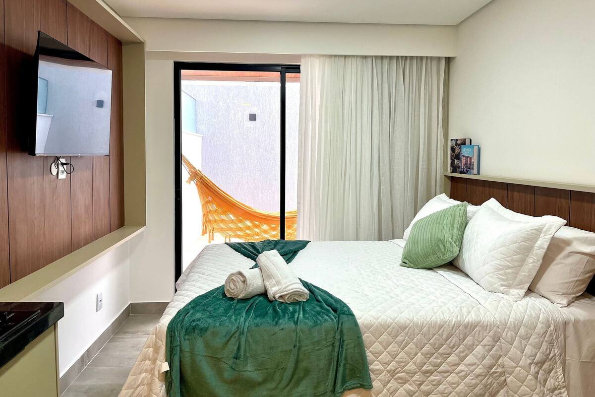 A hotel room with a bed, a TV mounted on the wall, a window with curtains, and a view of the outside.