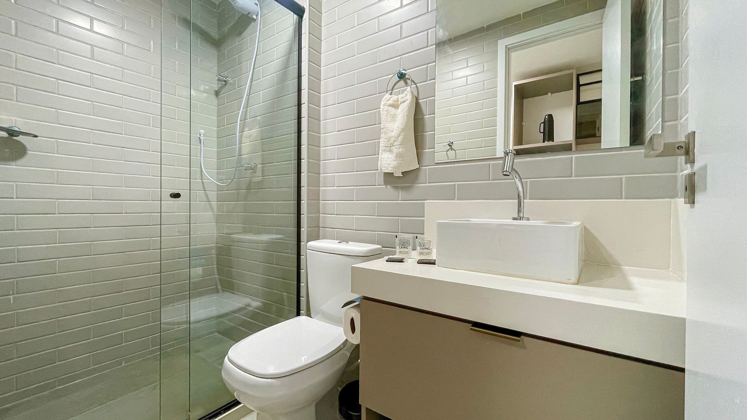 A bathroom with a glass-enclosed shower, a white toilet, a sink with a mirror above it, and a towel hanging on the wall.