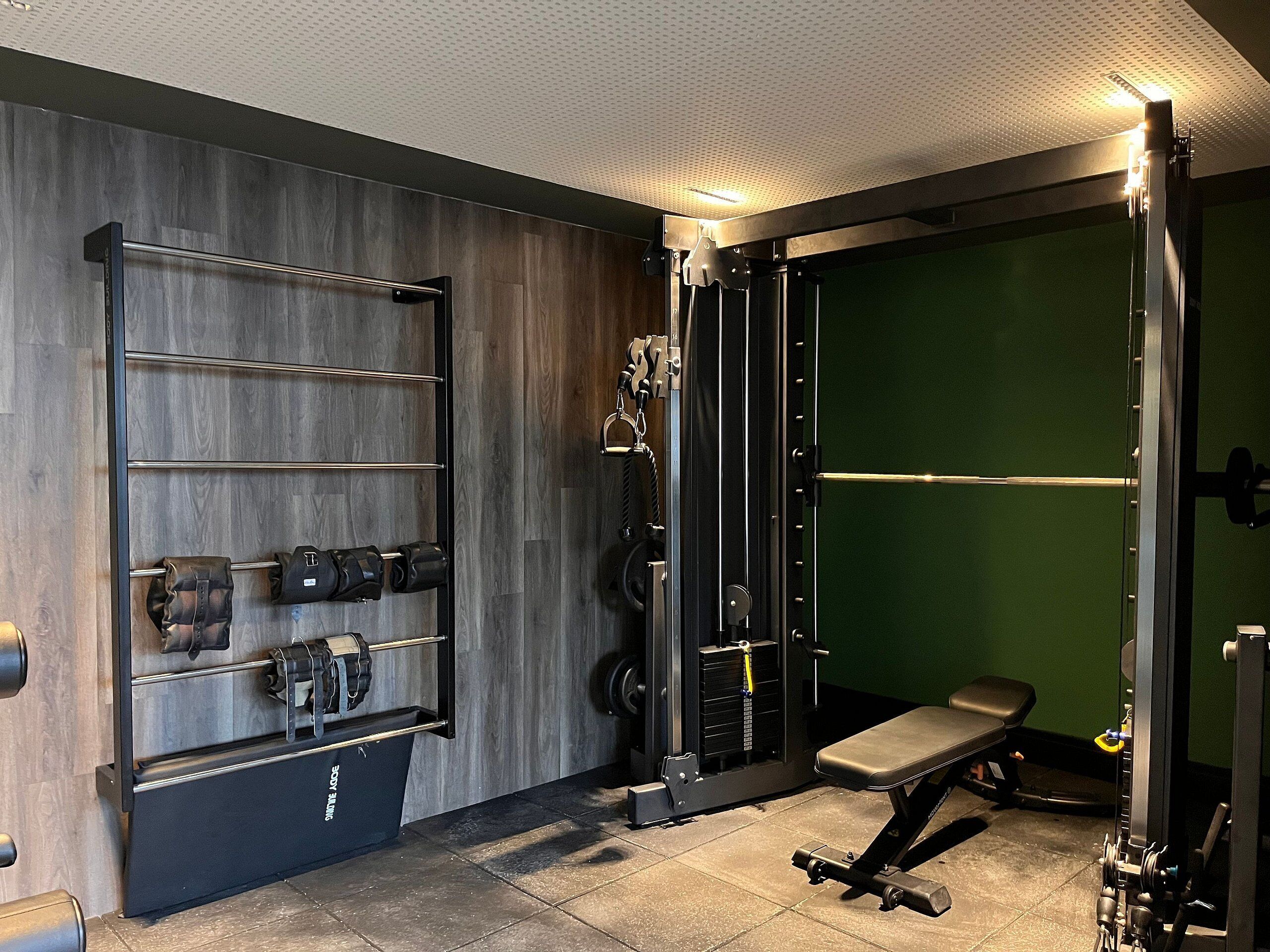 A gym with weightlifting equipment, a bench, and a wall-mounted rack.