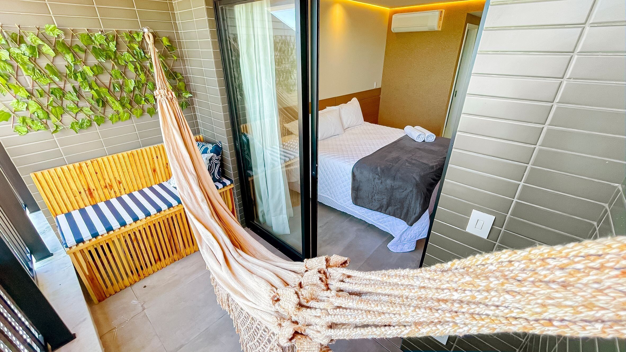 A hammock in a hotel room with a bed, a window, and a wall-mounted plant.