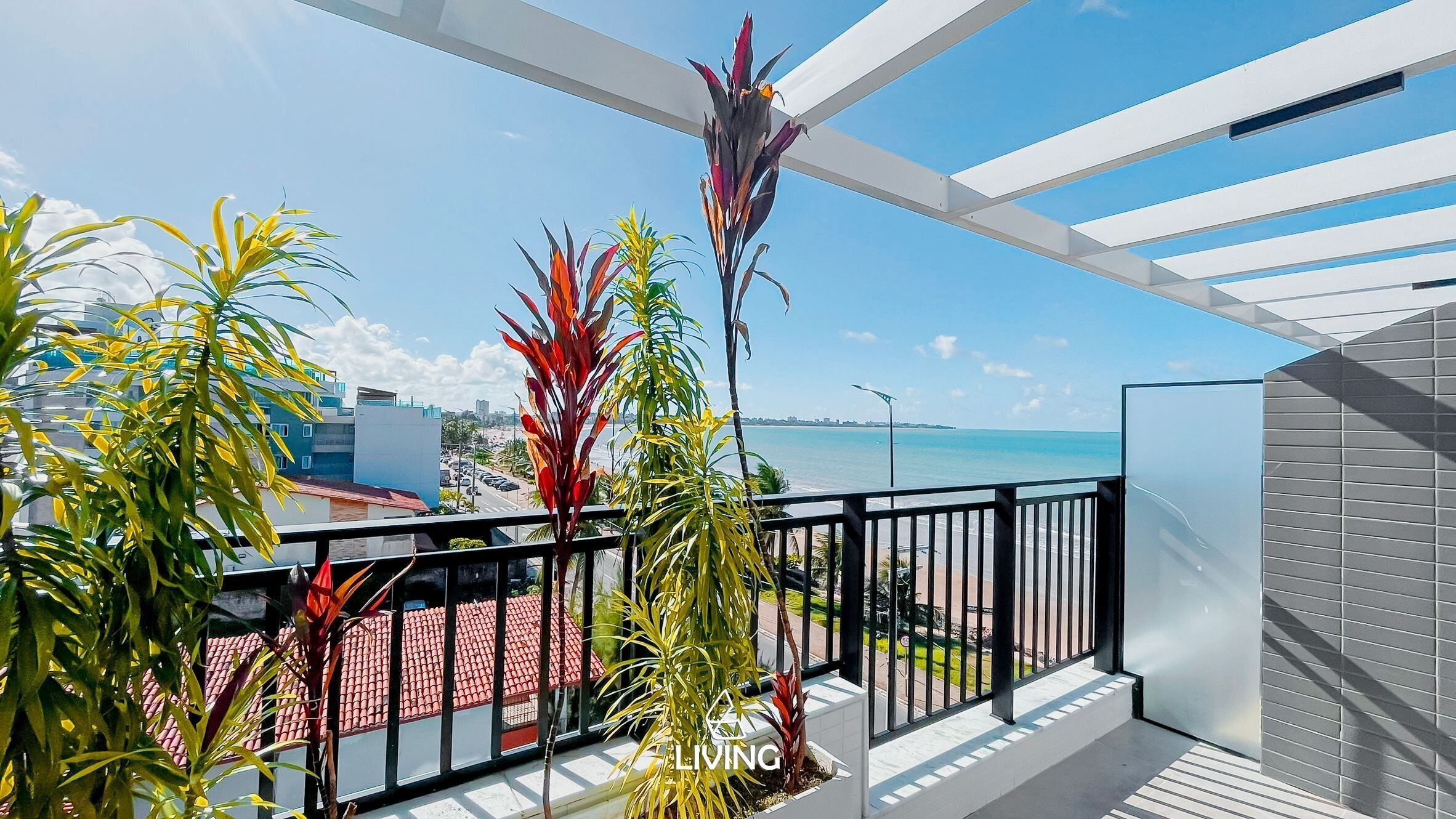 Un balcone con vista sul mare, piante tropicali e un edificio moderno sullo sfondo.