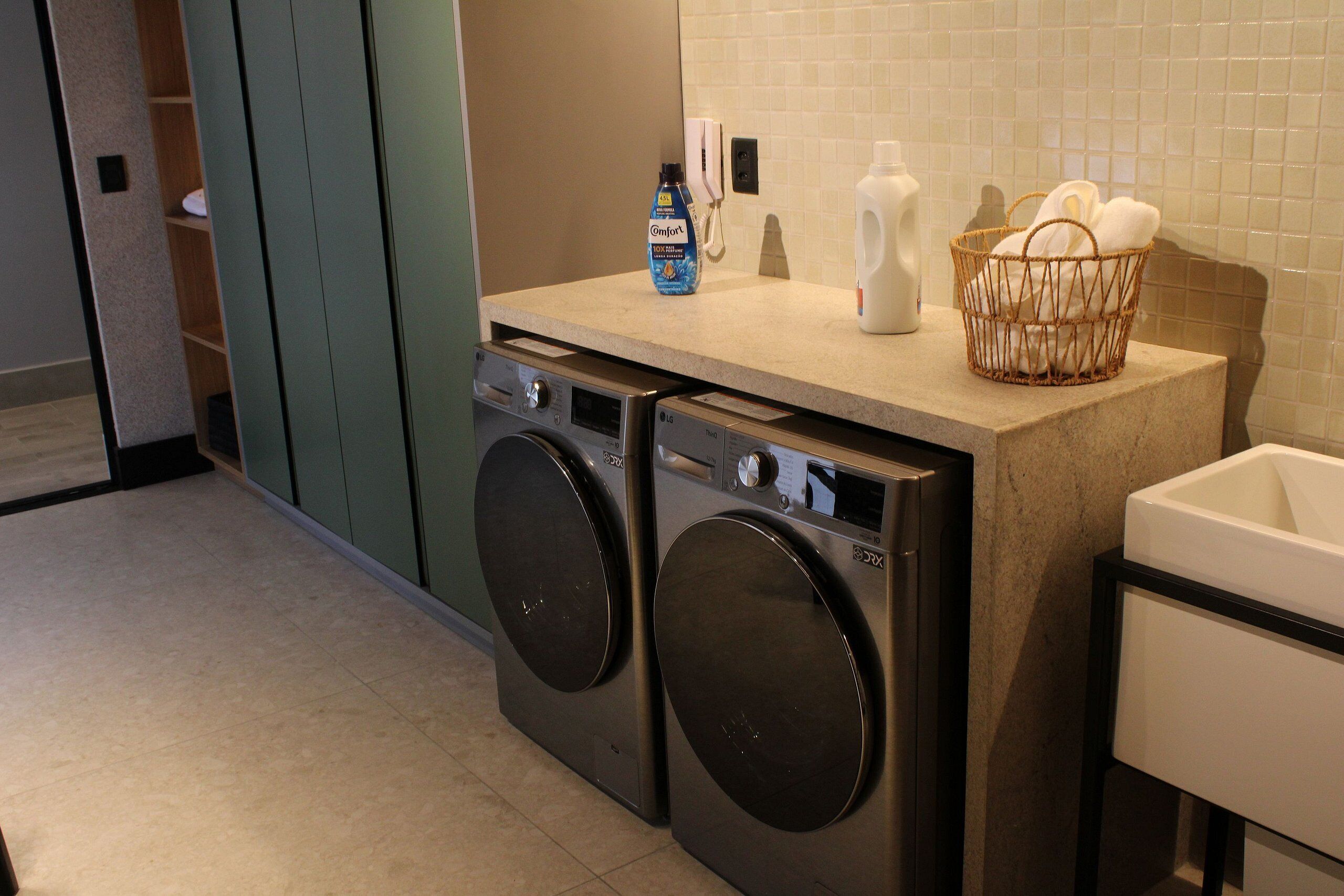 A laundry area with two front-loading washing machines, a bottle of Comfort dish soap, a white bottle, and a wicker laundry basket on a countertop.