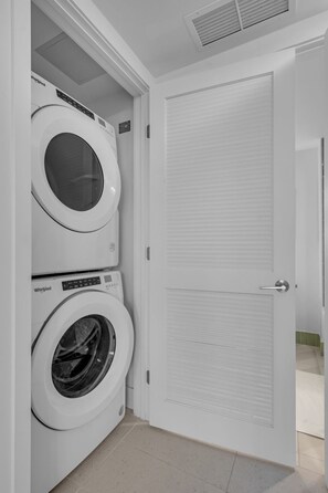 A laundry room with two stacked Whirlpool washers and dryers, a closed door with a vent, and a tiled floor. - Sunlit 1BR Condo In Downtown Miami (Miami)