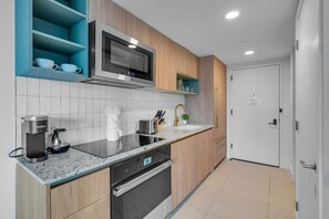 A modern kitchen with a built-in microwave, a coffee maker, and a toaster. There is a sink with a gold faucet and a small potted plant on the counter. - Sunlit 1BR Condo In Downtown Miami (Miami)
