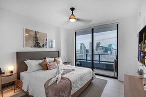 A modern bedroom with a large bed, a city view through a sliding door, and a ceiling fan.