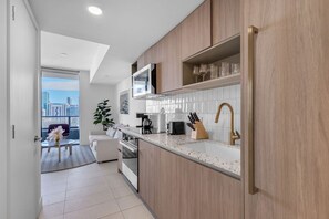 A modern kitchen with wooden cabinets, a stainless steel sink, and a city view through the window. - Bright & Breezy 1 Bed Unit With Water & City Views (Miami)