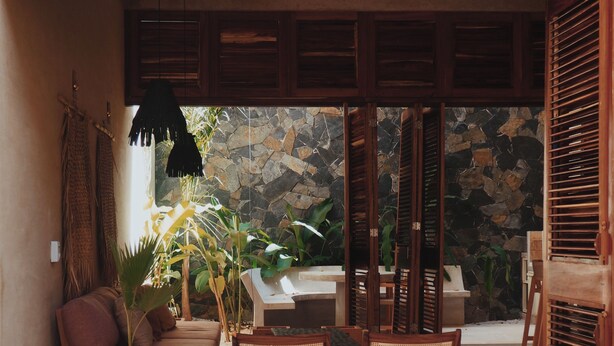 A cozy outdoor seating area with wicker furniture, a stone wall, and a view of the garden. - Casa Boga - Comfortable designer house in La Punta (Brisas de Zicatela)