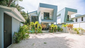 Een modern herenhuis met een oprit van grind en tropische planten.