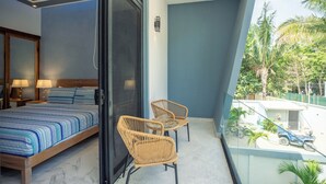 Een balkon met een bed, twee rieten stoelen en uitzicht op een zwembad en groen.