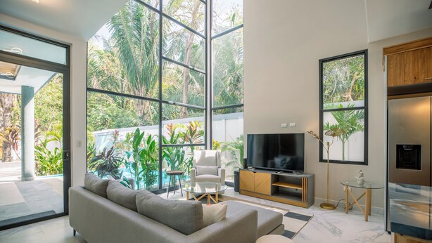 Een moderne woonkamer met een grote televisie, comfortabele zithoek en uitzicht op weelderige begroeiing.
