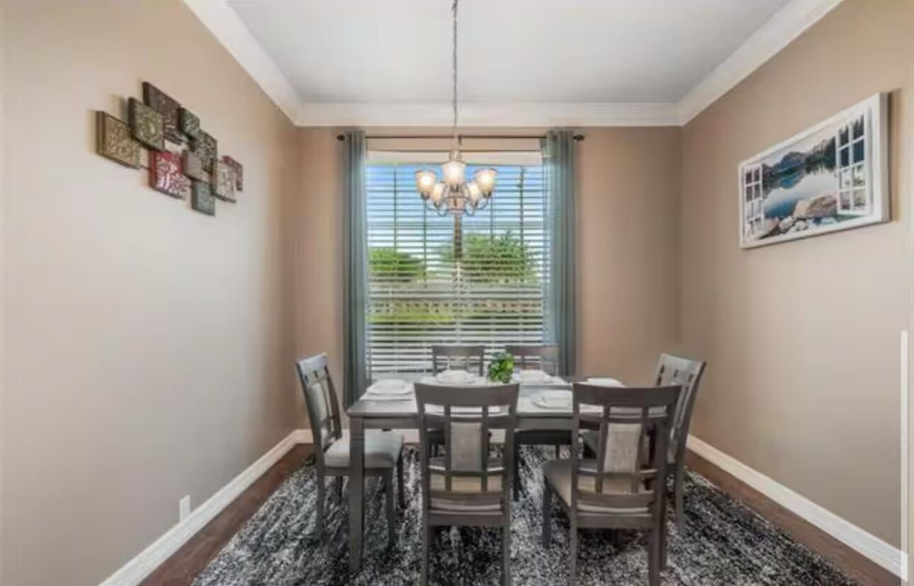 A dining room with a chandelier, a table set for four, and a window with blinds.