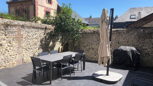 A patio with a table and chairs, a covered umbrella, and a stone wall.