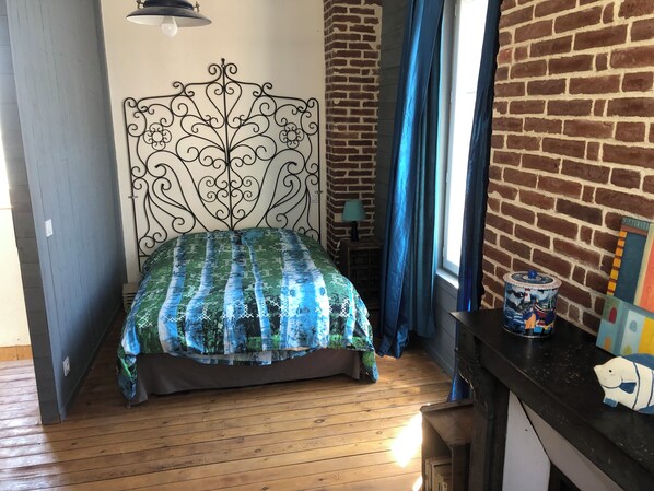 A bedroom with a bed, a brick wall, a window with curtains, and a nightstand with a lamp. - Beautiful, large family home. In the heart of Honfleur. 2-12 people (Honfleur)