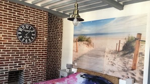 A bedroom with a brick fireplace, a beach-themed wall mural, and a colorful bedspread.